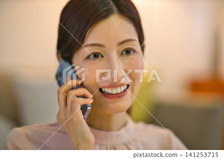 一位四十多歲的女性晚上在房間裡放鬆，看著她的智慧型手機。 141253715