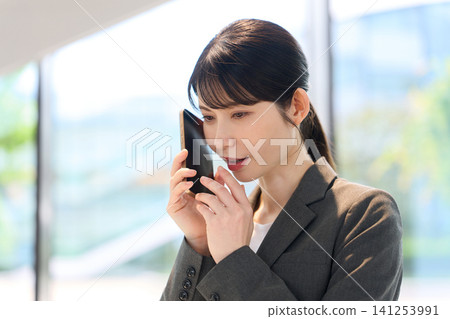 A businesswoman making secret phone calls during work hours. A businesswoman making secret phone calls during work hours. 141253991