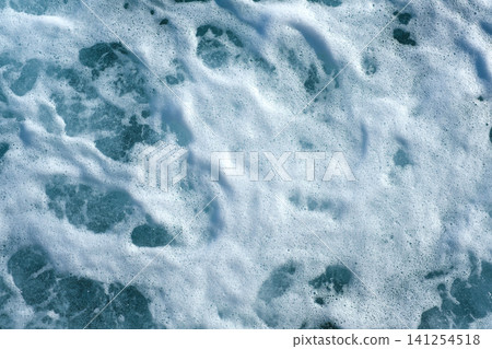 Ocean water surface displays white foam and bubbles, creating a textured appearance against a deep blue background of the sea 141254518