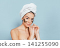 Young woman applying mask to face, towel wrapped around head 141255090