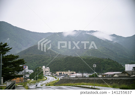 在陰雨綿綿的天空下,山巒景色盡收眼底,雨雲在山脈上空飄蕩,一條濕漉漉的道路延伸到遠方。 在陰雨綿綿的天空下,山巒景色盡收眼底,雨雲在山脈上空飄蕩,一條濕漉漉的道路延伸到遠方。 141255637
