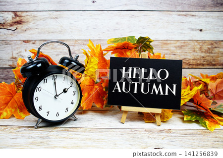 Hello Autumn text with alarm clock and maple leaf decoration on wooden background Hello Autumn text with alarm clock and maple leaf decoration on wooden background 141256839