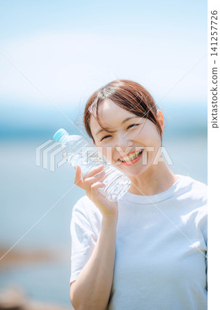 A woman holding a plastic bottle smiles with her eyes narrowed. A woman holding a plastic bottle smiles with her eyes narrowed. 141257726