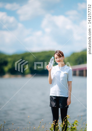 一名女子在湖邊拿著一個塑膠瓶。 一名女子在湖邊拿著一個塑膠瓶。 141257732