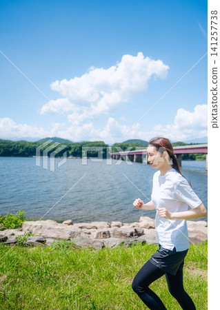 一位女子奔跑,背景是湖泊和橋樑。 一位女子奔跑,背景是湖泊和橋樑。 141257738