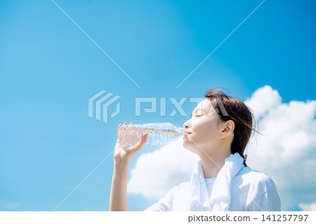 A woman drinking water under the summer sky A woman drinking water under the summer sky 141257797