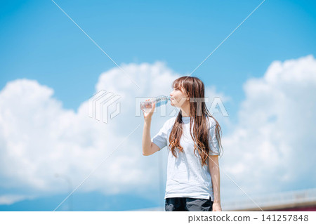 一張女子全身照,她正在喝水,背景是一座橋。 一張女子全身照,她正在喝水,背景是一座橋。 141257848