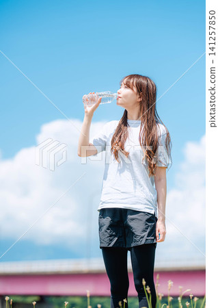 一張女子全身照,她正在藍天下用塑膠瓶喝水。 一張女子全身照,她正在藍天下用塑膠瓶喝水。 141257850