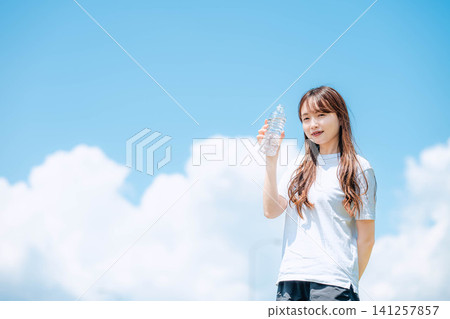 A refreshing woman holding up a plastic bottle under the blue sky. A refreshing woman holding up a plastic bottle under the blue sky. 141257857
