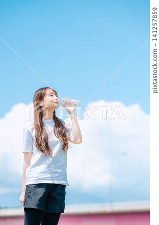 一位女子一邊喝水一邊抬頭望著天空。 一位女子一邊喝水一邊抬頭望著天空。 141257859