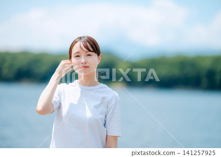 一位女子在湖光山色的襯托下,輕撫秀發,臉上洋溢著微笑。 一位女子在湖光山色的襯托下,輕撫秀發,臉上洋溢著微笑。 141257925