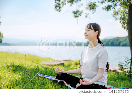一位女子在湖邊靜坐冥想，鏡頭捕捉到她的側臉。 141257975