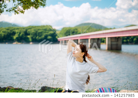 A woman relaxing by the lake with a view of mountains and a bridge. A woman relaxing by the lake with a view of mountains and a bridge. 141257985