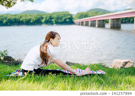 A woman doing a forward bend stretch on the grass. A woman doing a forward bend stretch on the grass. 141257994