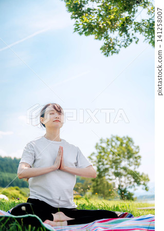 A woman meditating with her hands clasped in prayer in the shade of a tree. A woman meditating with her hands clasped in prayer in the shade of a tree. 141258007