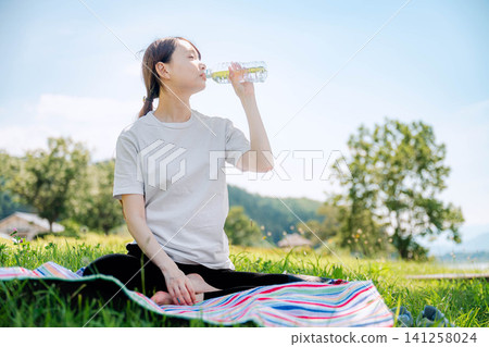 A woman drinks water from a plastic bottle with her eyes closed. A woman drinks water from a plastic bottle with her eyes closed. 141258024