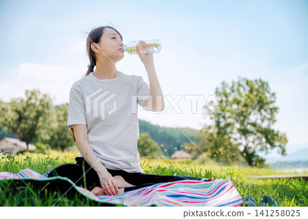 A woman sits on the grass and rehydrates. A woman sits on the grass and rehydrates. 141258025