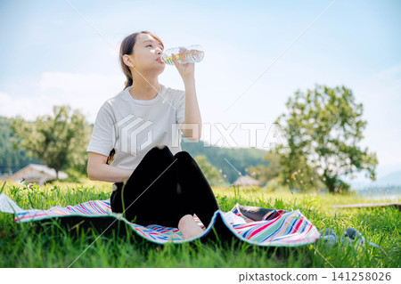 A woman rehydrating using a picnic mat. A woman rehydrating using a picnic mat. 141258026