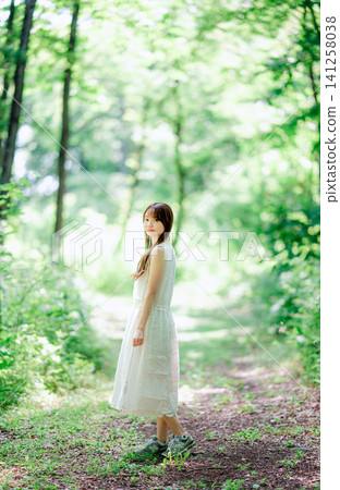 A woman in a white dress walks along a forest path and looks back. 141258038