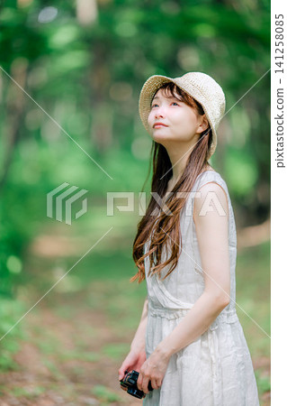 A woman in a straw hat looks up at the trees. A woman in a straw hat looks up at the trees. 141258085