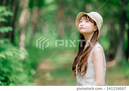A woman in a straw hat looks up in the forest. A woman in a straw hat looks up in the forest. 141258087