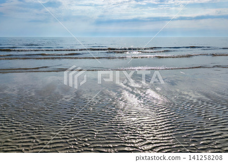 Rippled Baltic Seashore Beach Sand at Low Tide with Gentle Waves and Sun Reflection on Calm Sea Coast View Rippled Baltic Seashore Beach Sand at Low Tide with Gentle Waves and Sun Reflection on Calm Sea Coast View 141258208