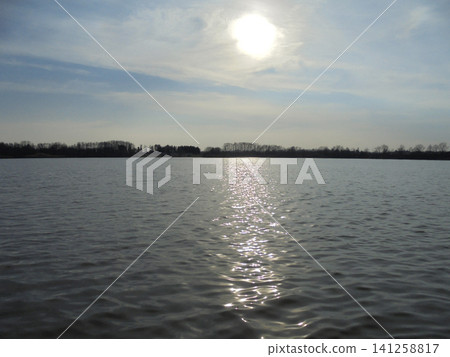 Vast wavy water surface and half-covered sun over horizon. Vast wavy water surface and half-covered sun over horizon. 141258817