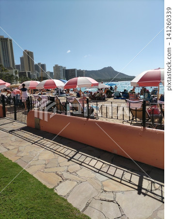 The lively crowds of people with parasols along the beach, with Diamond Head visible in the distance. The lively crowds of people with parasols along the beach, with Diamond Head visible in the distance. 141260339