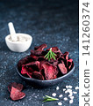 Homemade crispy vegan beet slices snack in a black bowl. Dark blue textured background with coarse sea salt, rosemary sprigs and copy space. Perfect for healthy diet and organic food marketing 141260374