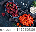 Baked beet and carrot slices with coarse sea salt scented rosemary. Vegan diet food idea and recipe. Healthy homemade beetroot and carrot chips in plate and ingredients on dark blue background. Copy 141260389