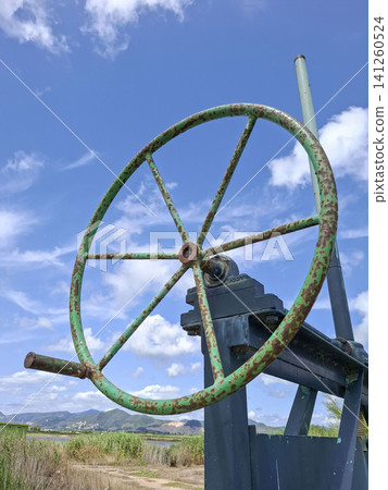 The image shows a close up of a weathered handwheel valve. This valve is used to control water levels in the irrigation canals of the Bomba rice fields in Pego under a blue sky. The image shows a close up of a weathered handwheel valve. This valve is used to control water levels in the irrigation canals of the Bomba rice fields in Pego under a blue sky. 141260524