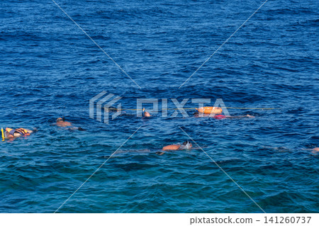 Group of snorkelers in life jackets swim in clear blue ocean water, with coral reef visible beneath the surface, showcasing marine life 141260737