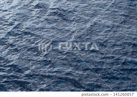 Dark blue water surface shows gentle ripples and reflections, creating a textured appearance in a natural aquatic setting Dark blue water surface shows gentle ripples and reflections, creating a textured appearance in a natural aquatic setting 141260857