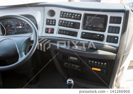 Interior of a truck cabin showing the dashboard with various controls, a steering wheel, and a digital display for navigation and audio systems Interior of a truck cabin showing the dashboard with various controls, a steering wheel, and a digital display for navigation and audio systems 141260908