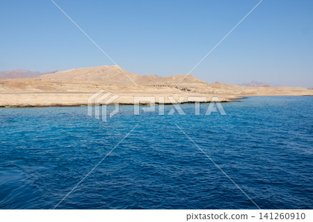 Coastal view with vibrant blue water and dry hills under a clear sky, highlighting the serene landscape and natural features of the region Coastal view with vibrant blue water and dry hills under a clear sky, highlighting the serene landscape and natural features of the region 141260910