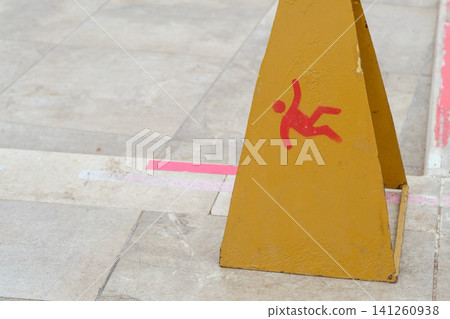 Yellow caution cone displays a red falling person symbol on a tiled floor, highlighting a slip hazard in an urban setting Yellow caution cone displays a red falling person symbol on a tiled floor, highlighting a slip hazard in an urban setting 141260938