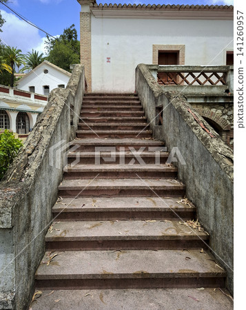The perspective shows a concrete staircase that is weathered and aged, leading up to an abandoned building in Borja sanatorium. The area is quiet and overgrown with plants. The perspective shows a concrete staircase that is weathered and aged, leading up to an abandoned building in Borja sanatorium. The area is quiet and overgrown with plants. 141260957