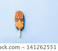 Healthy homemade plant-based chia seeds popsicle with raw carrot cake layer and chocolate coating with nuts. Minimalist flat lay on blue background. Chia popsicle with chocolate, copy space 141262551
