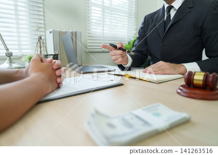 Lawyer explaining contract terms to client at desk with gavel and money Lawyer explaining contract terms to client at desk with gavel and money 141263516