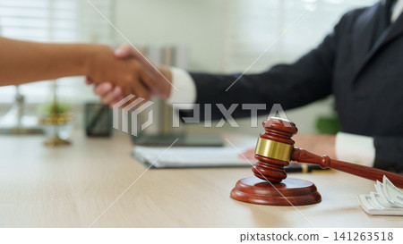 Lawyer shaking hands with client behind wooden gavel on desk for legal agreement Lawyer shaking hands with client behind wooden gavel on desk for legal agreement 141263518