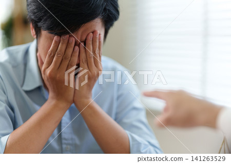 Stressed Asian businessman covering face during workplace accusation and conflict Stressed Asian businessman covering face during workplace accusation and conflict 141263529