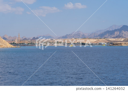Scenic coastal view of a resort town featuring mountains, clear blue water, and a bright sky in a desert landscape 141264032