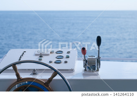 Boat steering wheel and control panel featuring throttle lever, with a clear view of calm ocean waters under bright daylight Boat steering wheel and control panel featuring throttle lever, with a clear view of calm ocean waters under bright daylight 141264110