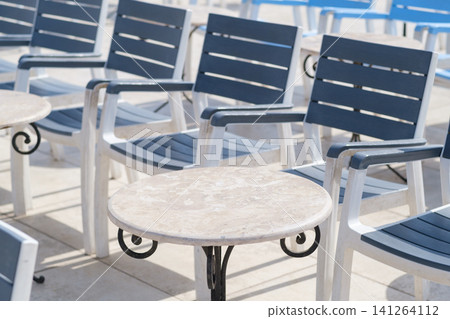 Outdoor seating area showcases several blue and white lounge chairs positioned around a small round table on a bright sunny day Outdoor seating area showcases several blue and white lounge chairs positioned around a small round table on a bright sunny day 141264112