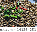 A close-up background of crispy deep-fried crickets garnished with kaffir lime leaves and red chilies. Popular Thai exotic snack, street food, and alternative insect protein concept. 141264251