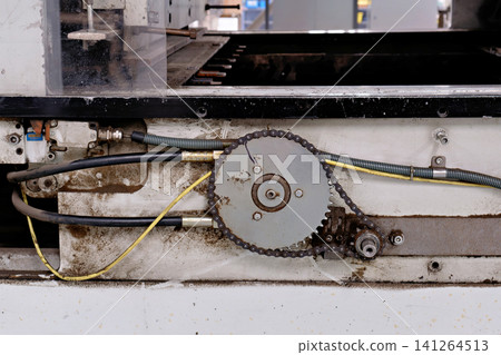 Close view of a mechanical chain drive sprocket and hydraulic hoses on machinery Close view of a mechanical chain drive sprocket and hydraulic hoses on machinery 141264513