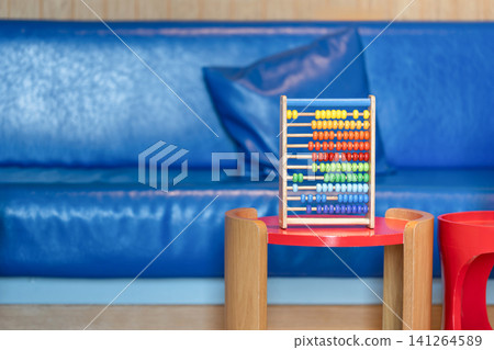 Colorful wooden abacus toys placed on children tables with a cozy blue seating area in the background. Colorful wooden abacus toys placed on children tables with a cozy blue seating area in the background. 141264589