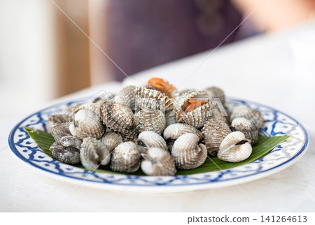 Blanched blood cockles on a green banana leaf. The fresh shellfish are served in a traditional Thai ceramic dish. Blanched blood cockles on a green banana leaf. The fresh shellfish are served in a traditional Thai ceramic dish. 141264613