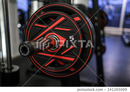 Close-up view of a black and red weight plate marked with five kilograms on a barbell, set against a contemporary gym background Close-up view of a black and red weight plate marked with five kilograms on a barbell, set against a contemporary gym background 141265099