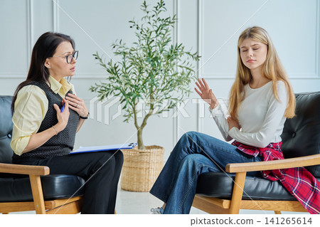 Rebellious teenage girl refusing to talk to female psychologist at therapy session 141265614